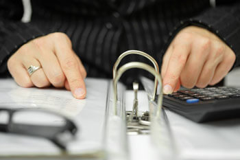 Eine Person liest in einem Aktenordner und hat einen Taschenrechner griffbereit.